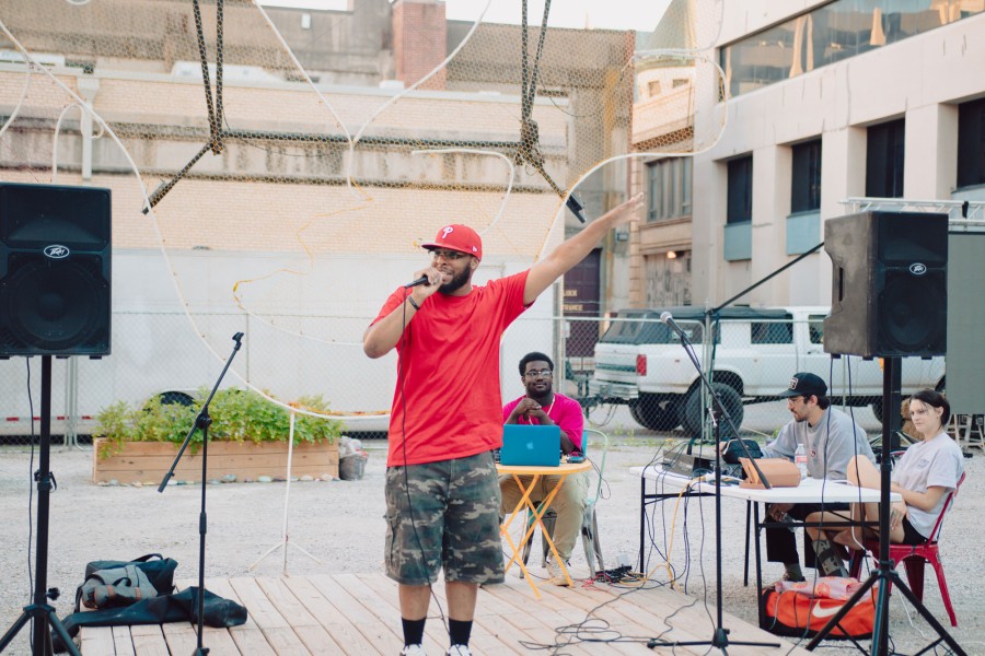 Man in red shirt and cap on stage holding microphone